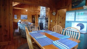 A wooden dining room with a long table set for four, a stone fireplace, and a blue cabinet with glassware. - Linekin Vista - 3BDR Waterfront Cottage on Linekin Bay with Private Beach! (East Boothbay)