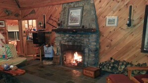 A cozy cabin interior with a stone fireplace, wooden walls, a television, and a sofa.