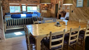 A cozy cabin interior with a wooden dining table, chairs, a sofa, and a kitchen area.