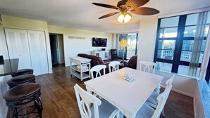 A spacious living area with a dining table, chairs, a ceiling fan, and a view of the outdoors through large windows. - Beautiful Sunsets On White Sandy Beach , Great Heated Pool - (Marco Island)
