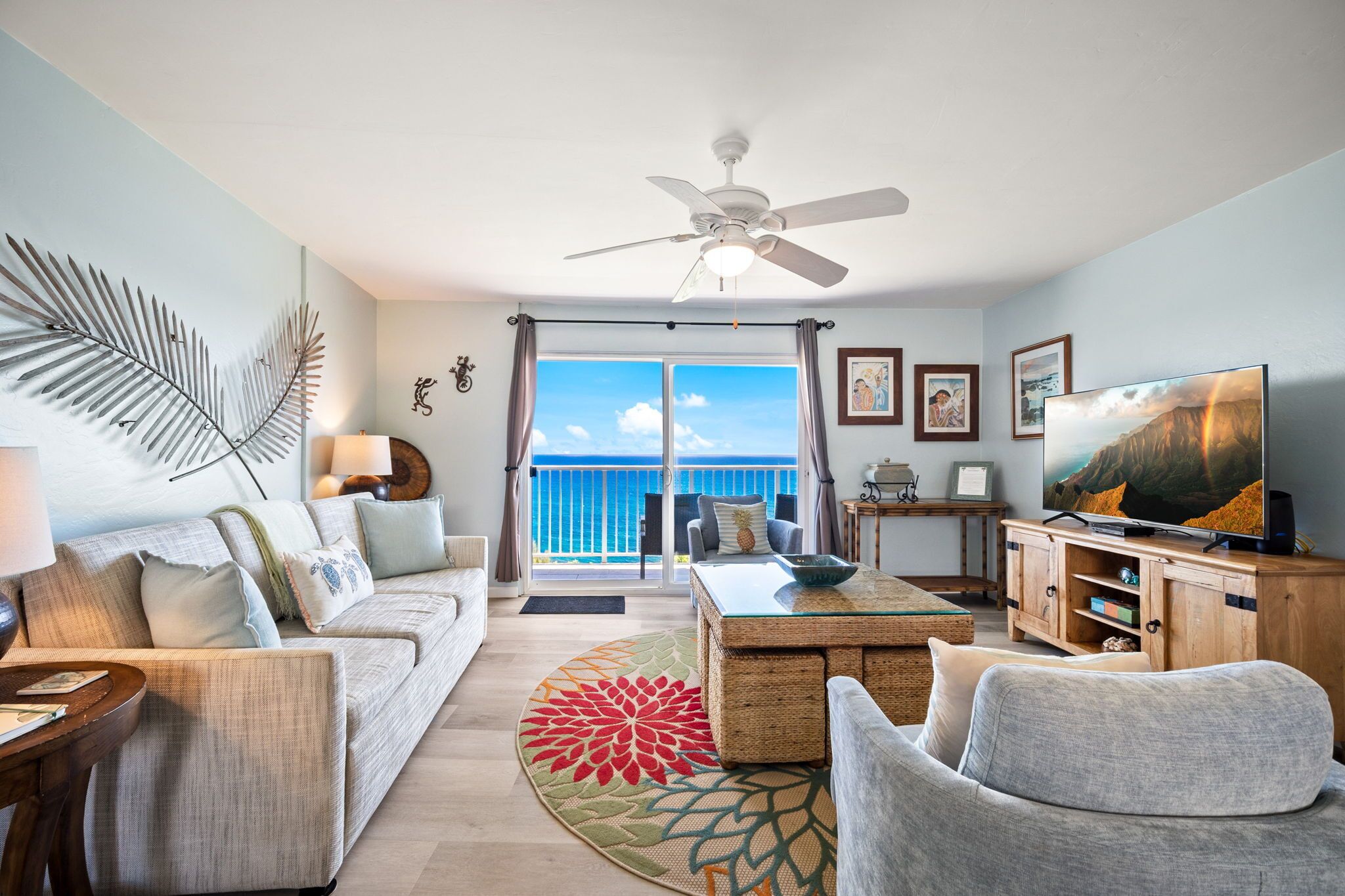 A living room with a sofa, armchair, coffee table, TV, and a balcony with a view.