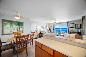 A spacious kitchen with a dining area, wooden furniture, and a large window offering a view of the ocean.