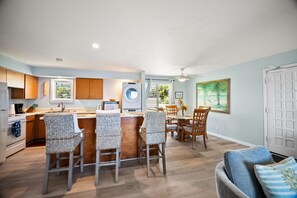 A kitchen with a central island, bar stools, a dining area with a table and chairs, and a view of the outdoors.
