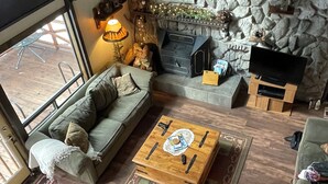A cozy living room with a stone fireplace, a sofa, a coffee table, and a television. - River Cottage (South Fork)