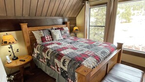 A bedroom with a wooden bed, a nightstand, a lamp, and a window with curtains. - River Cottage (South Fork)