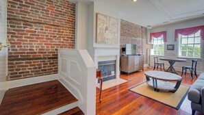 A spacious living area with a brick wall, a fireplace, a dining table, and a sofa. - The Carolina Suite - Heart of Historic Charleston (Charleston)
