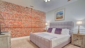 A bedroom with a brick wall, a bed with a headboard, bedside tables, and a lamp. - The Carolina Suite - Heart of Historic Charleston (Charleston)