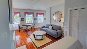 A spacious living room with hardwood flooring, a gray sofa, a round coffee table, and a dining area with a white table and chairs. - The Carolina Suite - Heart of Historic Charleston (Charleston)