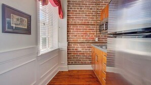 A narrow kitchen with a brick wall, wooden cabinets, and a stainless steel range hood. - The Carolina Suite - Heart of Historic Charleston (Charleston)