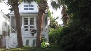 A white house with a porch, surrounded by palm trees and greenery. - Twin Palms Cottage (Tybee Island)