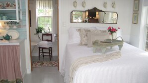 A cozy bedroom with a bed, a chair, a small table, and a mirror on the wall. - Twin Palms Cottage (Tybee Island)