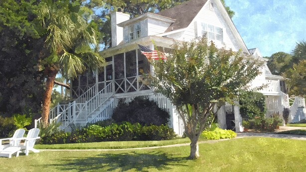 A large white house with a porch and American flag, surrounded by lush greenery and a well-maintained lawn. - Twin Palms Cottage (Tybee Island)