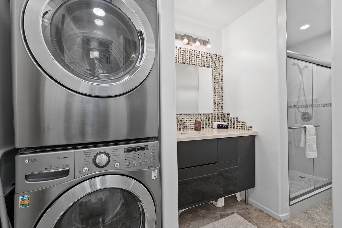 A modern bathroom with a built-in washer and dryer, a glass shower enclosure, and a vanity with a tiled backsplash.