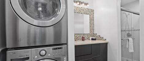A modern bathroom with a built-in washer and dryer, a glass shower enclosure, and a vanity with a tiled backsplash.