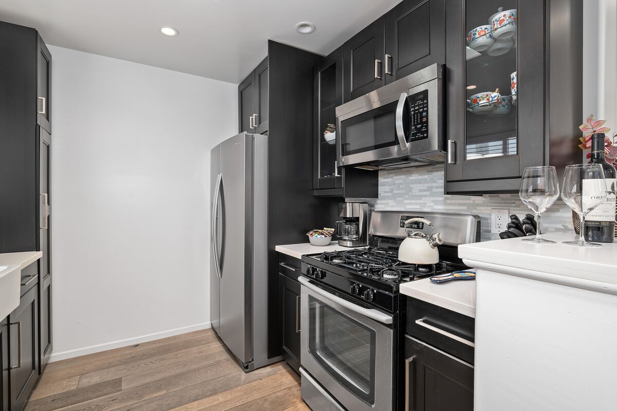 A modern kitchen with stainless steel appliances, dark cabinetry, and a white countertop.