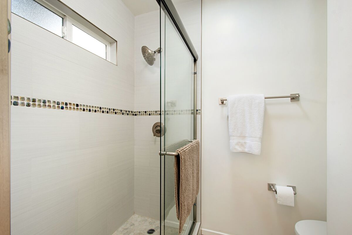 A modern bathroom with a glass shower enclosure, a white toilet, and a towel rack.