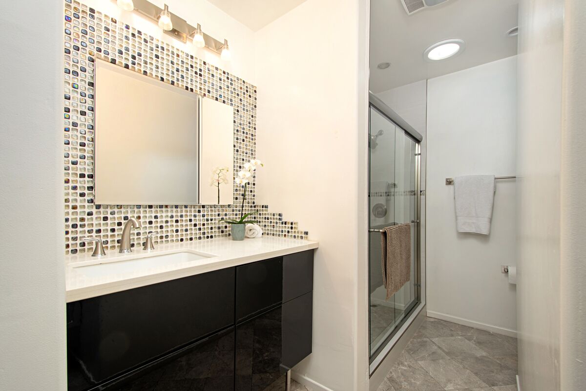 A modern bathroom with a large mirror, black cabinets, a white sink, and a glass shower enclosure.