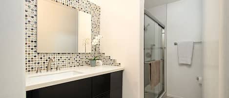 A modern bathroom with a large mirror, black cabinets, a white sink, and a glass shower enclosure.