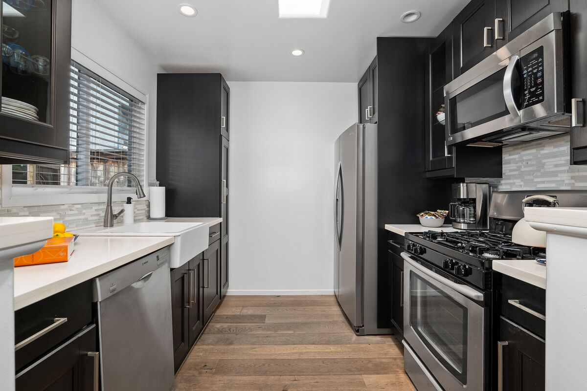 A modern kitchen with stainless steel appliances, a dishwasher, and a large window with blinds.