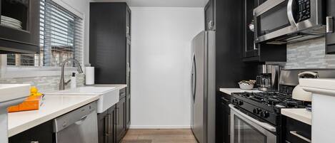 A modern kitchen with stainless steel appliances, a dishwasher, and a large window with blinds.