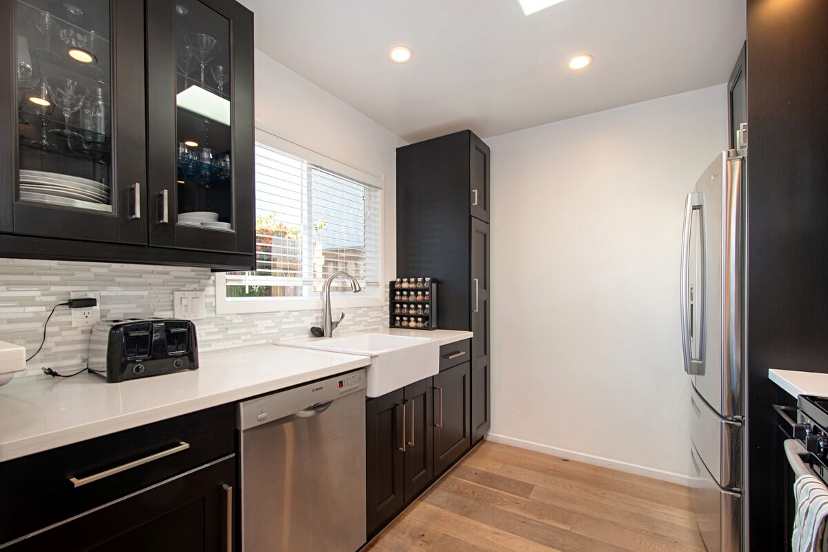 A modern kitchen with dark cabinets, a white countertop, a dishwasher, a double sink, and a stainless steel refrigerator.