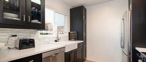 A modern kitchen with dark cabinets, a white countertop, a dishwasher, a double sink, and a stainless steel refrigerator.
