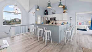 Une cuisine spacieuse dotée d’un îlot central, de tabourets de bar blancs et de luminaires suspendus.