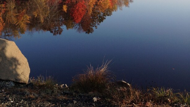 A calm lake with autumn foliage reflecting on the water, surrounded by rocky terrain and trees.