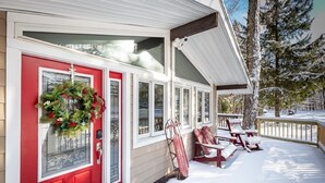 A house with a red door, a porch with snow-covered steps, and a snow-covered deck.