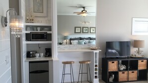 A modern kitchen with a microwave, toaster, and coffee maker. There are two stools and a TV in the living area. - Spectacular Ocean View! Great Location On 30A   King Bed ,Newly Remodeled! (Santa Rosa Beach)