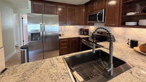 A kitchen with a stainless steel refrigerator, a microwave, a sink with a modern faucet, wooden cabinets, and a herringbone tile backsplash.