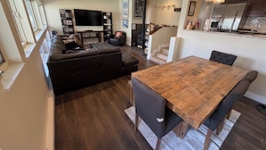 A modern living room with a large sofa, a wooden dining table, and a kitchen area with a refrigerator and stove.