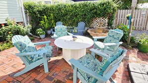 Eine Terrasse mit einem runden Tisch und vier passenden Stühlen, umgeben von einem Ziegelboden und einem Holzzaun.