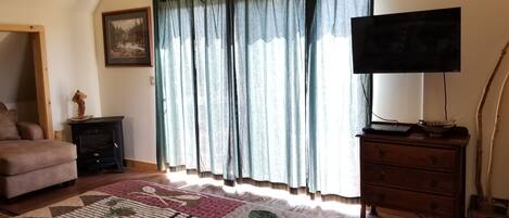A living room with a sofa, a fireplace, a television, and a large window with curtains.