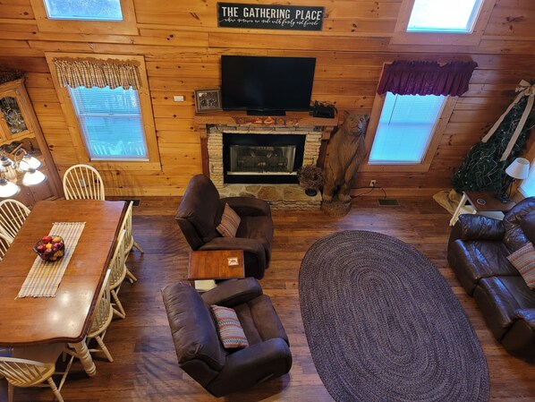 A cozy cabin interior with a dining area, a fireplace, a television, and a Christmas tree.