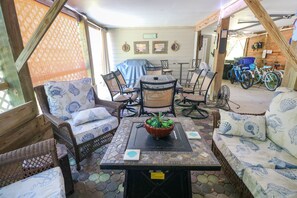 Un patio couvert aménagé avec des meubles en osier, une table centrale ornée d’une plante et, au fond, des vélos.