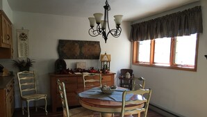 Un coin repas comprenant une table ronde, des chaises en bois, un lustre, une fenêtre avec des rideaux et un élément décoratif mural.