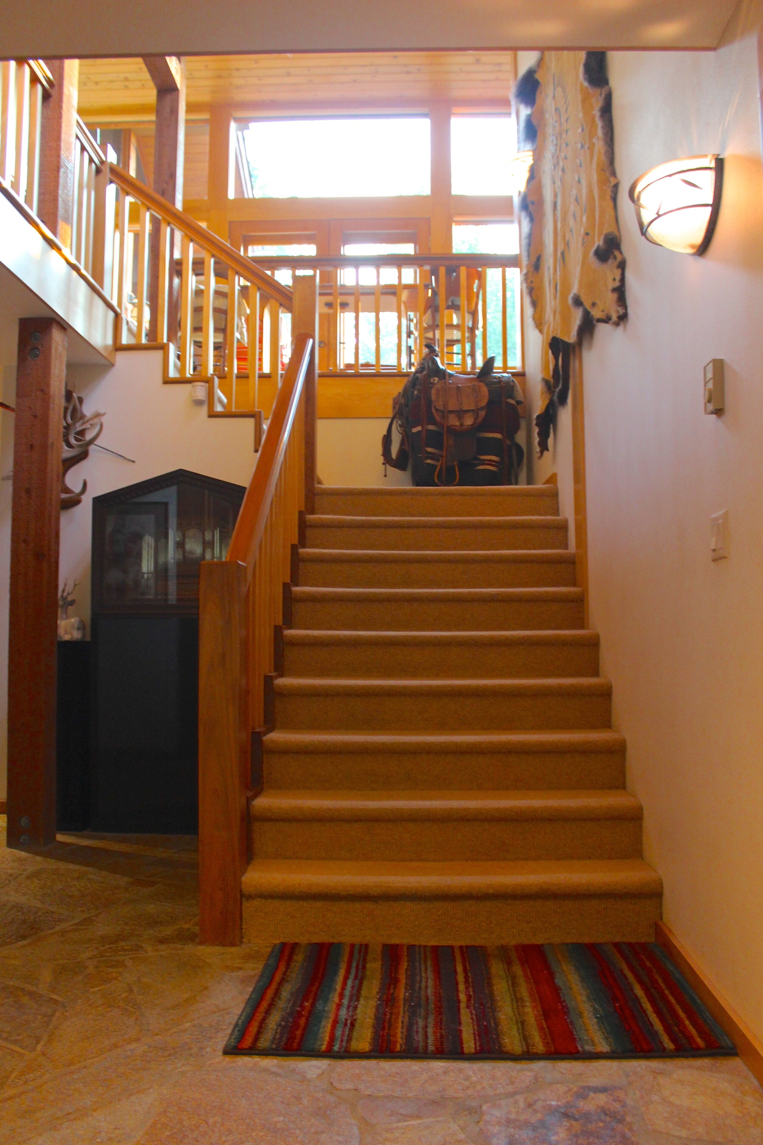 A wooden staircase with a handrail, leading to a second-floor landing with a view of the outdoors.