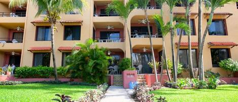 A multi-story hotel with balconies, palm trees, and a central pathway.