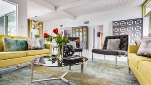 Uma sala de estar moderna com um sofá amarelo, uma poltrona preta e uma mesa de centro de vidro.