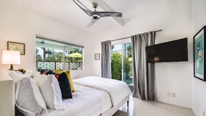 Quarto moderno com cama, ventilador de teto, TV e janelas amplas com cortinas.