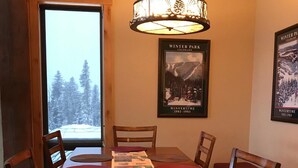 A dining area with a wooden table, four chairs, and a view of a snowy landscape through a glass door. - 2 Masters, Private Hot Tub, Superb Views - Close to WP Resort Skiing, Biking (Winter Park)