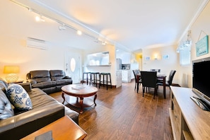 A living room with a sofa, coffee table, and TV stand. There is a kitchen area with a dining table and chairs. - OB Pier 1 - Steps to beach and restaurants (San Diego)