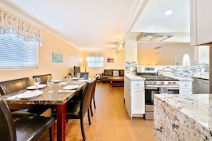A modern kitchen with a marble countertop, a dining area with a table set for four, and a living area with a sofa and coffee table. - OB Pier 1 - Steps to beach and restaurants (San Diego)