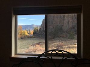 Enjoy a serene view of the surrounding landscape from this room's window, featuring a grassy field and a rocky cliff in the distance.