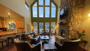 A spacious living area with a stone fireplace, large windows, and a cozy seating arrangement. - Gorgeous riverfront, 4-BR (2-master suite) home! (Southfork)