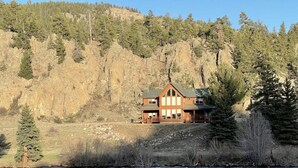 A lodge with a two-story structure, a balcony, and a view of a river and forested hillside. - Gorgeous riverfront, 4-BR (2-master suite) home! (Southfork)