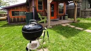 Una casetta di legno con un tetto viola, un barbecue in primo piano e una sedia verde all'esterno.
