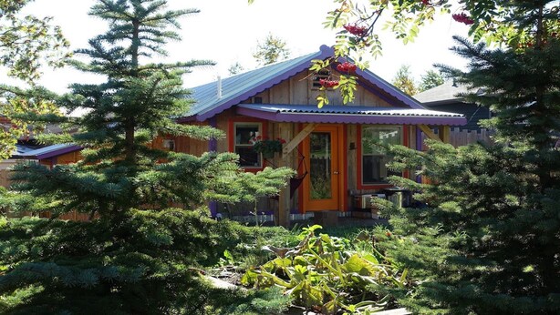 Una casa di legno con tetto viola e un portico anteriore, circondata da alberi sempreverdi.