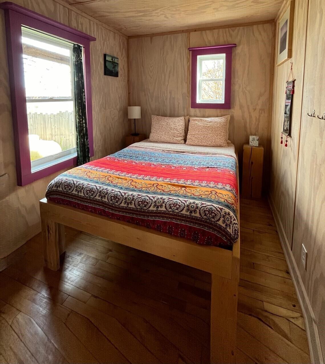 Une pièce aux murs lambrissés, avec un lit, une fenêtre et une petite table de chevet.